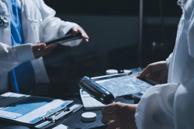 Two doctors and a female nurse meet at a table in the hospital, collaborating on medical tasks using laptops and computers