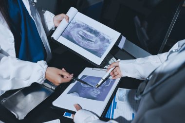 Two doctors and a female nurse meet at a table in the hospital, collaborating on medical tasks using laptops and computers