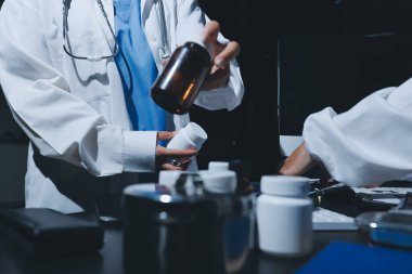Two doctors and a female nurse meet at a table in the hospital, collaborating on medical tasks using laptops and computers