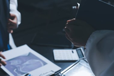Two doctors and a female nurse meet at a table in the hospital, collaborating on medical tasks using laptops and computers