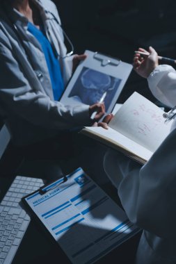 Two doctors and a female nurse meet at a table in the hospital, collaborating on medical tasks using laptops and computers
