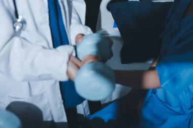 Fizyoterapist, halter egzersizinde bir kadına yardım ediyor.