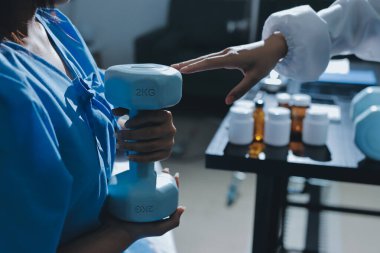 Fizyoterapist, halter egzersizinde bir kadına yardım ediyor.