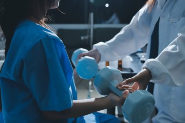 Fizyoterapist, halter egzersizinde bir kadına yardım ediyor.