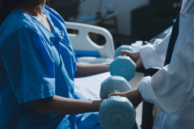 Fizyoterapist, halter egzersizinde bir kadına yardım ediyor.