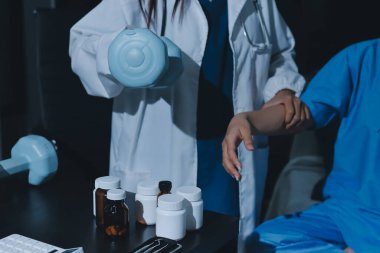 Fizyoterapist, halter egzersizinde bir kadına yardım ediyor.