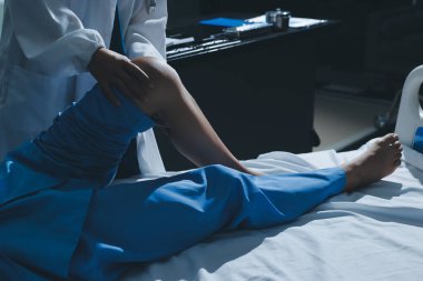 Hastane odasında yaralı bir kadının ayak bileğini inceleyen ve destekleyen doktor, burkulma ya da kırık için tıbbi yardım ve tedavi sunuyor.