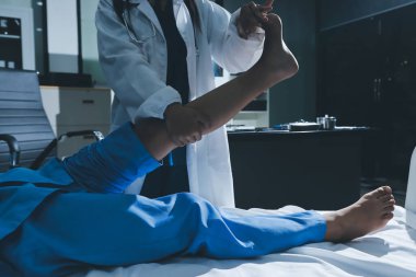 Hastane odasında yaralı bir kadının ayak bileğini inceleyen ve destekleyen doktor, burkulma ya da kırık için tıbbi yardım ve tedavi sunuyor.