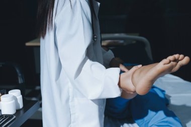 Hastane odasında yaralı bir kadının ayak bileğini inceleyen ve destekleyen doktor, burkulma ya da kırık için tıbbi yardım ve tedavi sunuyor.