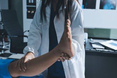 Hastane odasında yaralı bir kadının ayak bileğini inceleyen ve destekleyen doktor, burkulma ya da kırık için tıbbi yardım ve tedavi sunuyor.