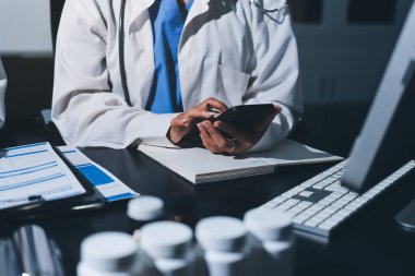 Two doctors and a female nurse meet at a table in the hospital, collaborating on medical tasks using laptops and computers