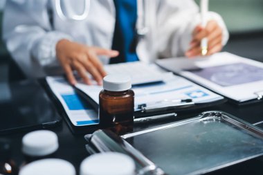 Two doctors and a female nurse meet at a table in the hospital, collaborating on medical tasks using laptops and computers