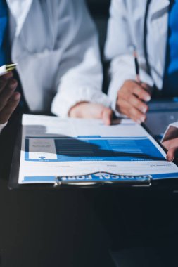 Two doctors and a female nurse meet at a table in the hospital, collaborating on medical tasks using laptops and computers