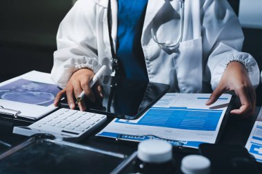 Two doctors and a female nurse meet at a table in the hospital, collaborating on medical tasks using laptops and computers