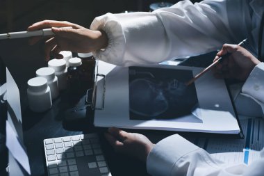 Two doctors and a female nurse meet at a table in the hospital, collaborating on medical tasks using laptops and computers