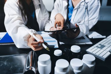 Two doctors and a female nurse meet at a table in the hospital, collaborating on medical tasks using laptops and computers