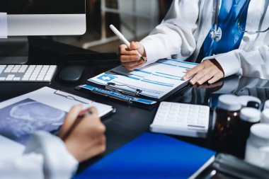 Two doctors and a female nurse meet at a table in the hospital, collaborating on medical tasks using laptops and computers