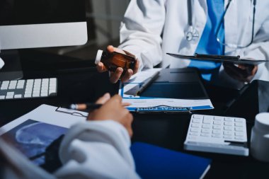 Two doctors and a female nurse meet at a table in the hospital, collaborating on medical tasks using laptops and computers