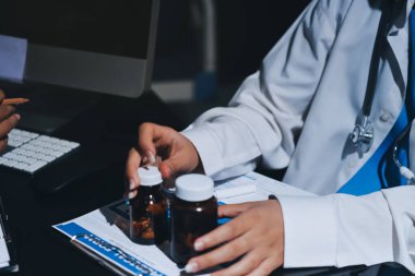 Two doctors and a female nurse meet at a table in the hospital, collaborating on medical tasks using laptops and computers