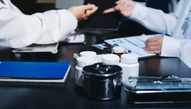 Two doctors and a female nurse meet at a table in the hospital, collaborating on medical tasks using laptops and computers