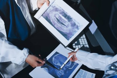 Two doctors and a female nurse meet at a table in the hospital, collaborating on medical tasks using laptops and computers