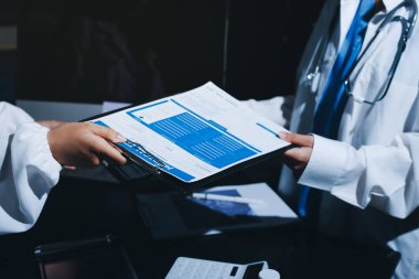 Two doctors and a female nurse meet at a table in the hospital, collaborating on medical tasks using laptops and computers