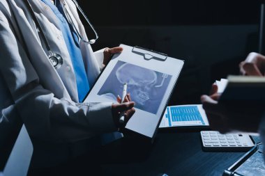 Two doctors and a female nurse meet at a table in the hospital, collaborating on medical tasks using laptops and computers