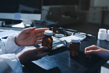 Elinde ilaç şişesi olan kadın doktor hastanın yan etkileri için ilaç kalitesini kontrol ediyor ve hasta bilgilerini hastanede kaydediyor. tıbbi ve sağlık hizmetleri kavramı