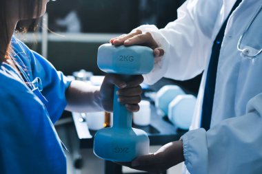 Fizyoterapist, halter egzersizinde bir kadına yardım ediyor.