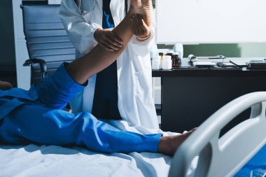 Hastane odasında yaralı bir kadının ayak bileğini inceleyen ve destekleyen doktor, burkulma ya da kırık için tıbbi yardım ve tedavi sunuyor.