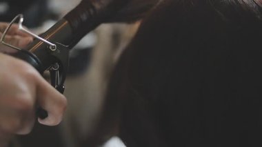 Usta kadın kuaför, kuaförde yıkandıktan sonra kızın saçını saç kurutma makinesiyle kurutur..