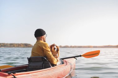Gölde kanoda köpeği olan bir adam. Kano kayığında spanyel ile gezen genç bir erkek, evcil hayvanlarla, arkadaşlıkla, macera köpekleriyle aktif boş zamanı var.