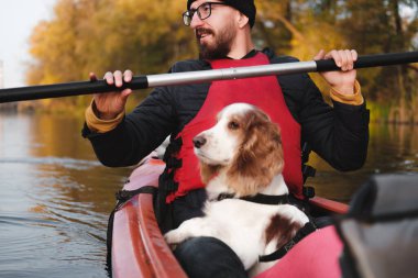 Mutlu adam spanyel köpeğiyle kanoda kürek çekiyor, güneşli sonbahar havası. Nehirde köpeklerle kanoya binmek, aktif hayvanlar, sağlıklı bir köpek ve bir serüvenin sahibi.