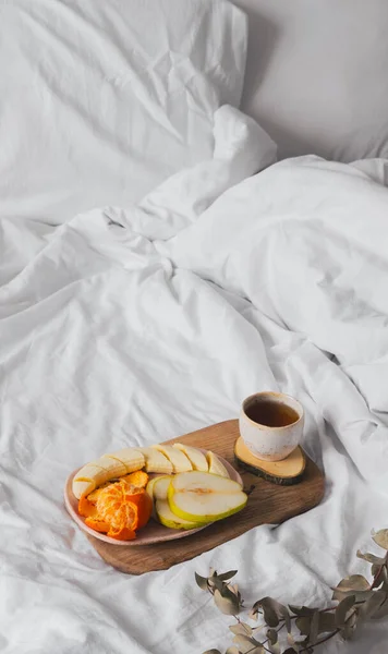 Tray with fruits and cup of tea in white clean bed. Mindful and quiet living, slow life, bed in breakfast concept, simple pleasures at home