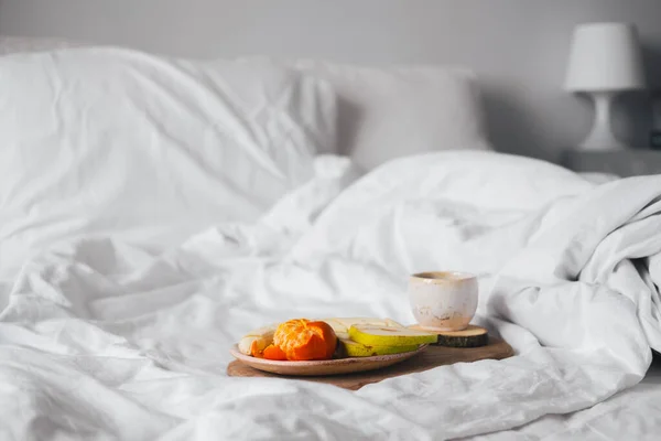 Tray with fruits and cup of tea in white clean bed. Mindful and quiet living, slow life, bed in breakfast concept, simple pleasures at home