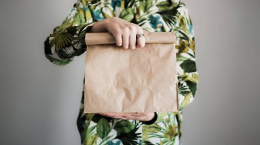 Kadın eli kahverengi bir kese kağıdını tutuyor, yakın çekim. Boş çevre dostu paket, hediye, sürpriz veya teslimat konsepti