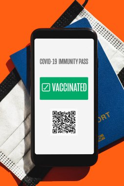 Covid 19 seyahat konsepti, dijital ve dokunulmazlık belgesi. Aşılanmış işaretli telefon ekranı, yüz maskesi ve parlak kırmızı arka planda biyometrik pasaport.