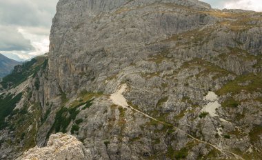 Dolomitlerin kireçtaşından geçtiği dar dağ patikaları, engebeli kayalık yamaçlardan geçen soluk dönüşlü yollar, seyrek alp bitkileri, yüksek uçurum duvarları, ağır bulutların altında kaybolan uzak vadiler, ham dağlık yalnızlık. Ital 'da Yakalandı