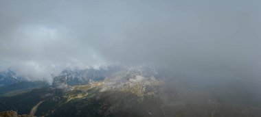 Yoğun fırtına bulutları ve dalgalı sis bulutları engebeli Dolomites tepelerinde kısmen kayalık tepeleri ve aşağıdaki sarmal alp patikalarını ortaya çıkarıyor. Işık, kuzey İtalya 'daki yüksek dağlık arazide dramatik bir kontrastlık yaratarak sisin içinden geçiyor..