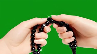 Yeşil arka planda siyah dua boncuklarını tutan ellerin yakın çekimi, dini bağlılığı, ruhaniliği ve İslam 'daki ibadeti simgeliyor..