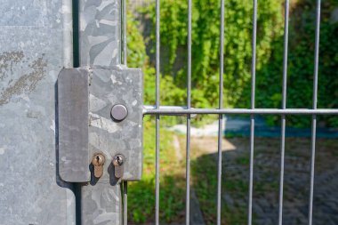 A plain steel gate is secured by two separate key cylinders fitted side by side on the same frame, the design looks sturdy and practical and the surfaces show use and light wear from passing hands