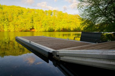 A compact pier holds a simple bench beside still water, reflections drift under the boards, the setting suggests rest and talk, an easy spot for watching light and gentle waves