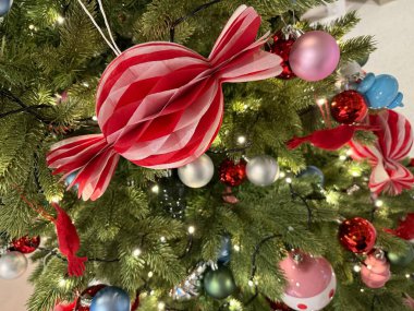 Kırmızı şeker süsü ve renkli takılarla süslenmiş Noel ağacı. Kutlama yaşam tarzı ve tasarım temaları için mükemmel neşeli bir tatil ortamı.