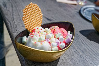 İçi siyah renkli, altın kaplama bir kasede kremalı dondurma ve üzerine de gökkuşağı şekerlemesi serpiştirilmiş ve yuvarlak bir gofret bulunur. Bu karışım yumuşak kafe ışığı altında neşeli ve parlak görünür.