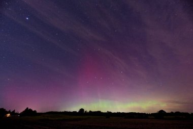 Aurora şeritleri Kollund, DK 'da yıldızlı bir gökyüzünde yumuşak pembe ve sarı ışık yayıldı. Ufuk boyunca hafif bir parıltı sürükleniyor, serin geceyi sakin bir gökyüzü gösterisine dönüştürüyor.
