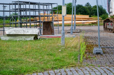 Geçici çitler bölgeyi işaretlerken, metal iskeleler bir projenin etrafında yükseliyor, özel bir inşaat aracı hazır duruyor, koniler ve direkler kılavuz hareketler ve tozlar havada hafifçe asılı duruyor