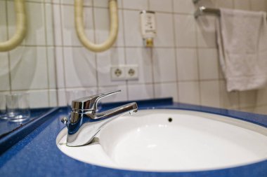 Beyaz bir seramik lavabo mavi destek sütununda duruyor. Etrafında da otel ya da servis alanı gibi görünen bir lavabo var. Musluk ve yüzey temiz ve kullanışlı..