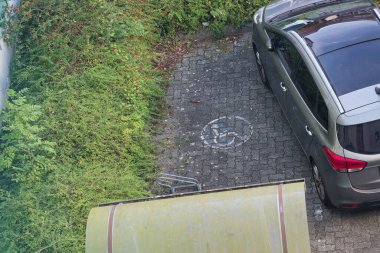 Bir araba eğri duruyor ve işaretli engelli park alanının sınırına asılıyor. Boyalı alan kısmen kapatılmış, sahne dikkatsiz park yerini gösteriyor ve engelli sürücüler için erişimi zorlaştırıyor..