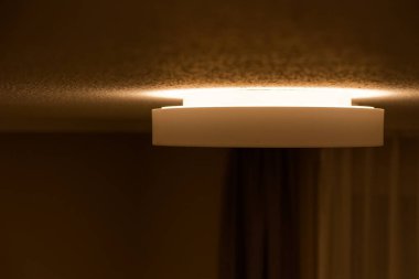 Yuvarlak bir ışıltı beyaz tavanın ortasında durur ve hafifçe yukarı doğru süzülür, cilalı vücut sakin ve asgari kalır oda dengeli ve berrak hissederken sabit bir parıltı altında.