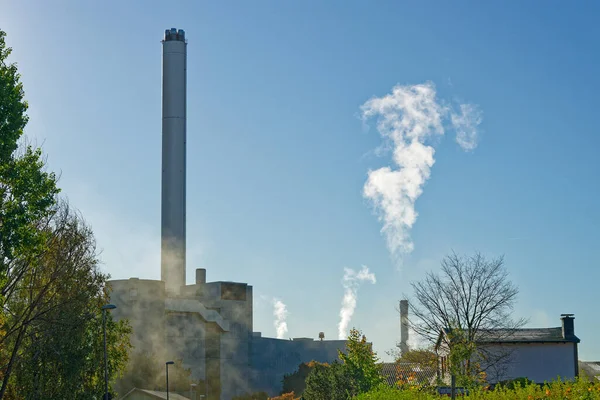 Stadtwerke Flensburg tesisi uzun egzoz yığınlarıyla serin gökyüzüne soluk bir duman salıyor. Geniş bahçe ve sabit duvarlar burayı düzenli ve düzenli hale getiriyor..
